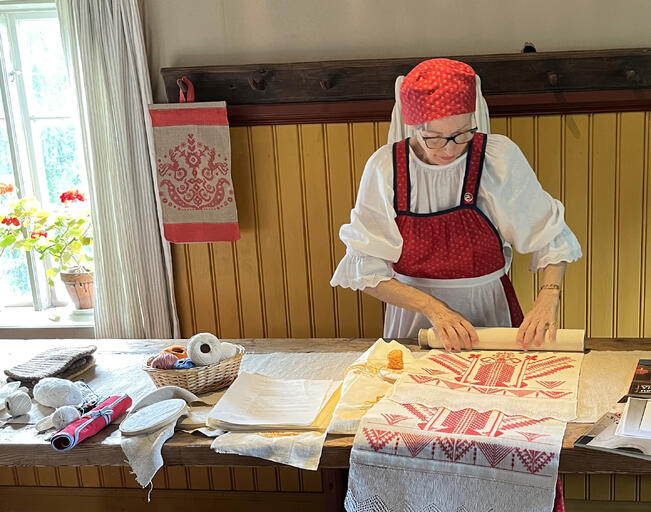 Helena Nurmela käärii auki etupistokirjottua käspaikkaa vuoden 2023 Karjalaisen käsityön päivänä.