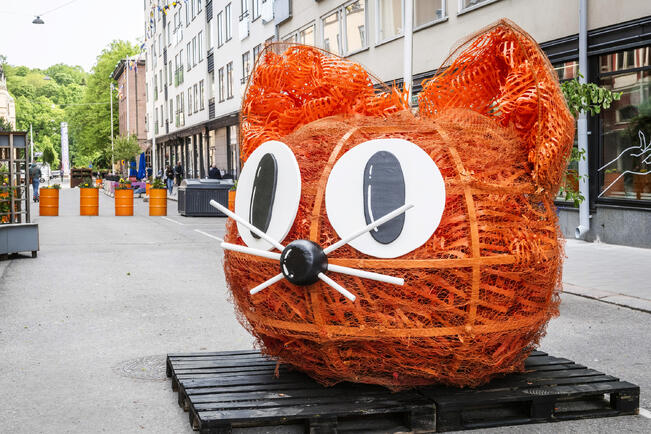 Lähes kokonaan kierrätysmateriaaleista valmistetussa veistoksessa on käytetty muun muassa karvaisen näköiseksi ryntättyä oranssia huomioaitaa.